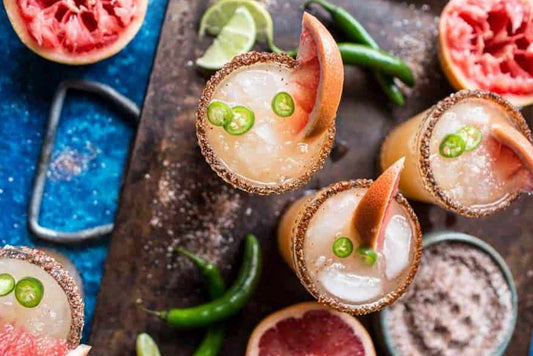 Spicy Grapefruit Margarita in glasses on wood board with red grapefruit garnish and spicy chili salt rims.