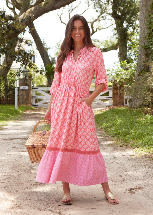 A brunette woman with her hand in a pocket of the Cabana Life sun protective Amelia Island Relaxed Maxi Dress holding a picnic basket outside.