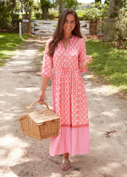 A brunette woman walking outside wearing the Cabana Life sun protective Amelia Island Relaxed Maxi Dress holding a picnic basket.