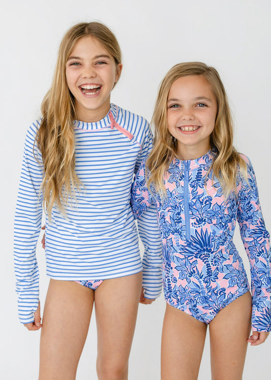 Blonde girls laughing while wearing the sun protective Girls Palm Beach 3-Piece Long Sleeve Rashguard Set and Girls Palm Beach Long Sleeve One-Piece from Cabana Life.