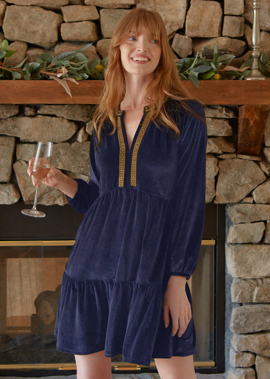 A redhead woman holding a champagne glass in front of a fireplace wearing the Cabana Life sun protective Navy Embroidered Velvet Tiered Dress. 