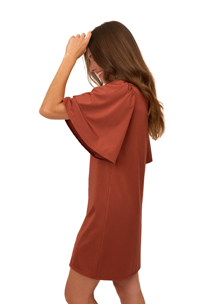 A brunette woman wearing Cabana Life's sun protective Copper Flutter Sleeve Shift Dress with her arm up to her head on a white background.