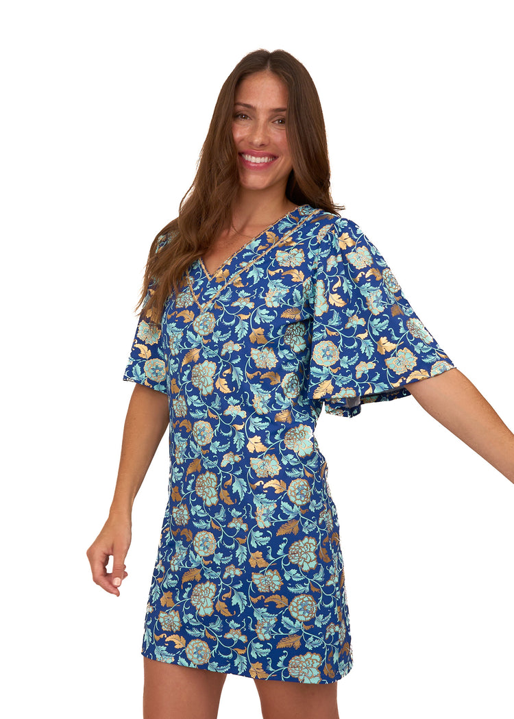 A brunette woman wearing the Cabana Life sun protective Navy Floral Metallic Embroidered Flutter Sleeve Shift Dress on a white background.