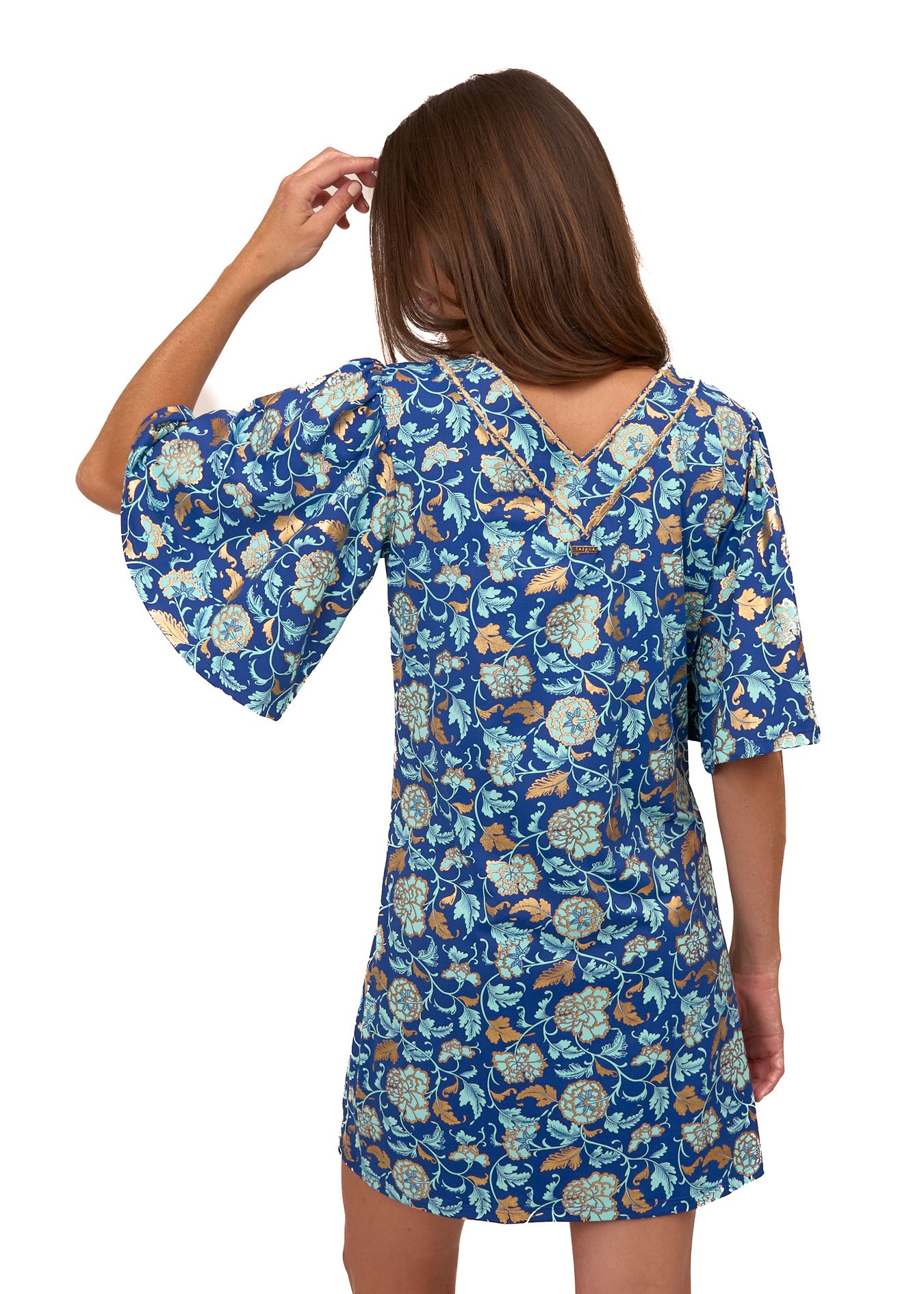 The back of a brunette woman wearing the Cabana Life sun protective Navy Floral Metallic Embroidered Flutter Sleeve Shift Dress on a white background.