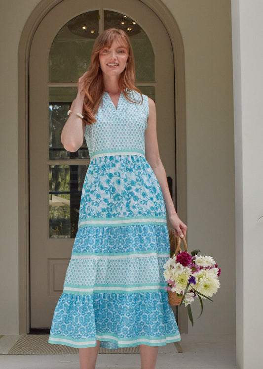 A redhead woman wearing the Cabana Life sun protective Rosemary Beach Sleeveless Tiered Maxi Dress and holding a bag of flowers in front of a house.