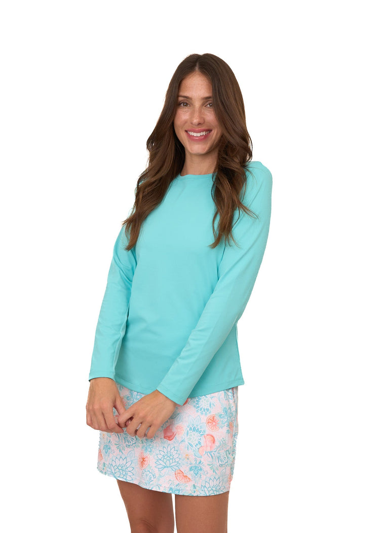 A brunette woman with her arms in front wearing the sun protective Aqua Performance Crewneck and Spritz 15" Skort from Cabana Life on a white background.