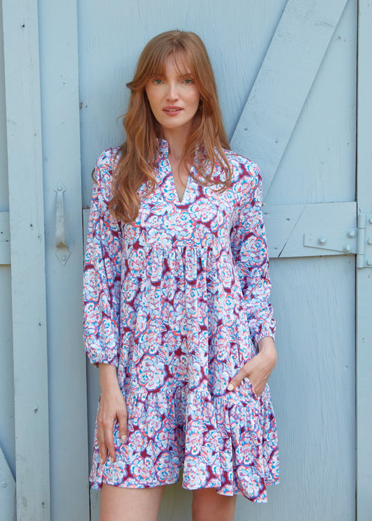 A redhead woman in front of a light blue door wearing the sun protective Cabana Life Camden Peony Relaxed Dress.