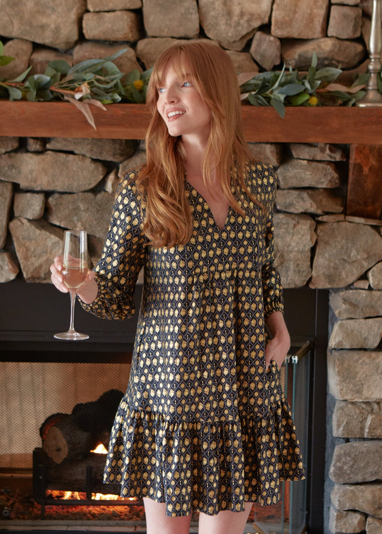 A redhead woman holding a glass of champagne and looking to the side while wearing the sun protective Cabana Life Black Metallic Relaxed Dress with her hand in her pocket.