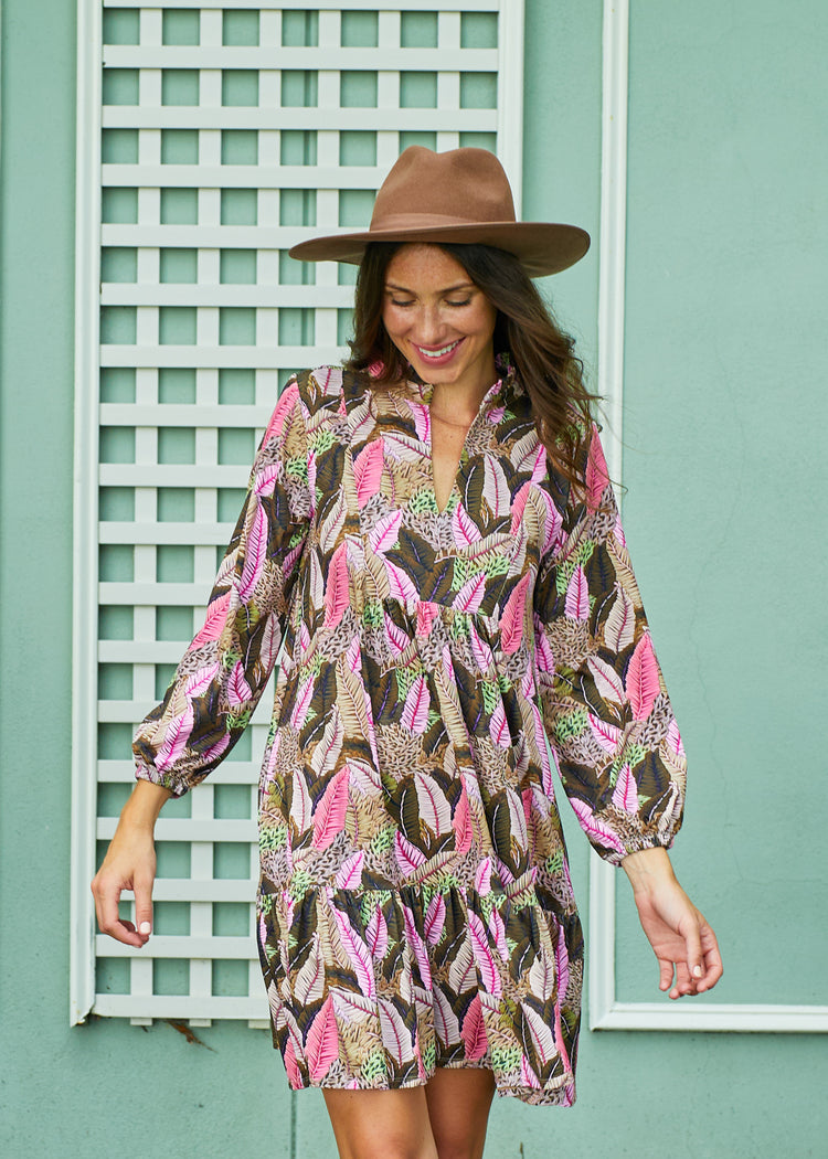 A brunette woman in front of a green building wearing Cabana Life's sun protective Myers Relaxed Dress and a hat while looking down.