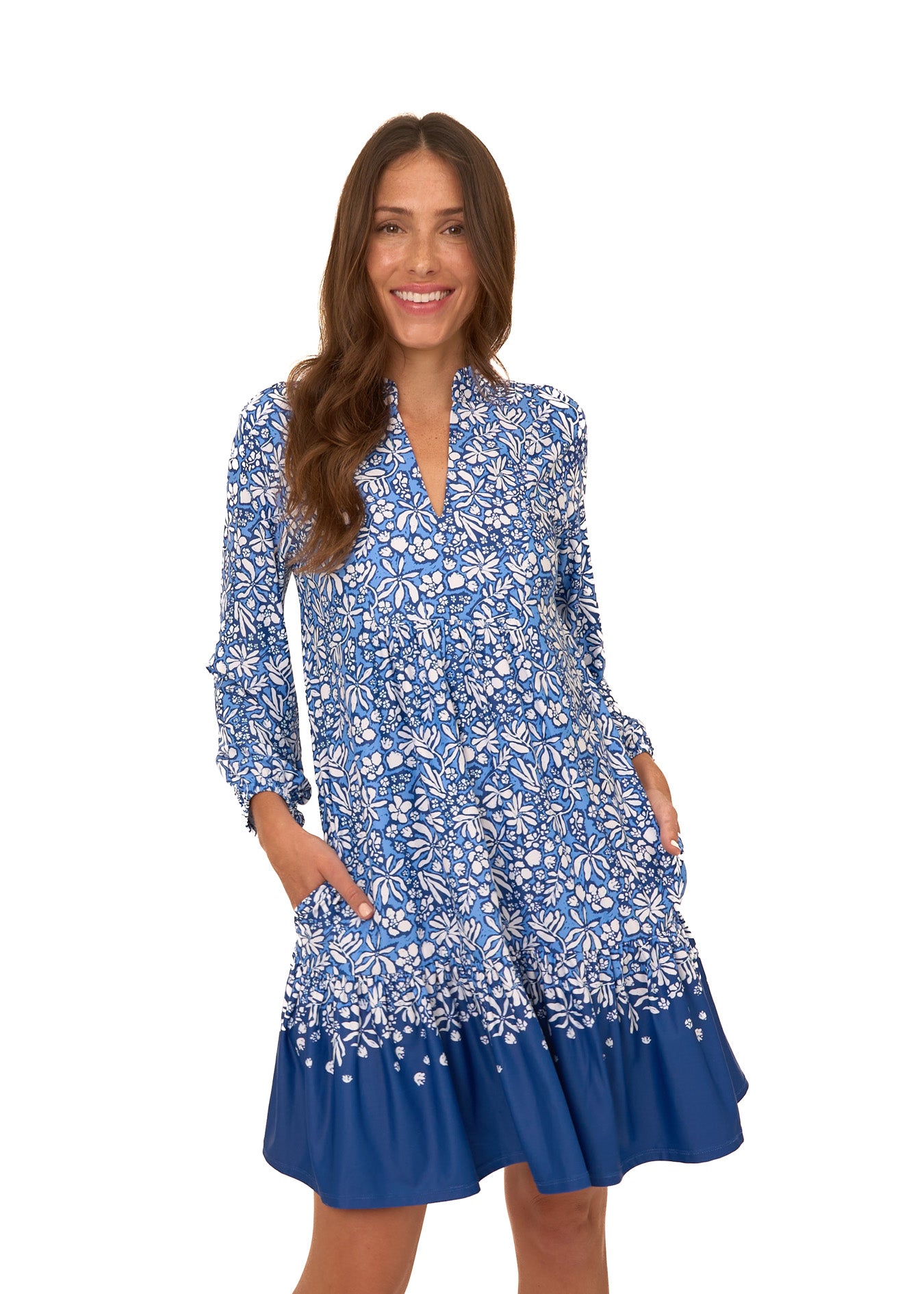 A brunette woman wearing Cabana Life's sun protective Seaside Floral Relaxed Dress with her hands in pockets on a white background.