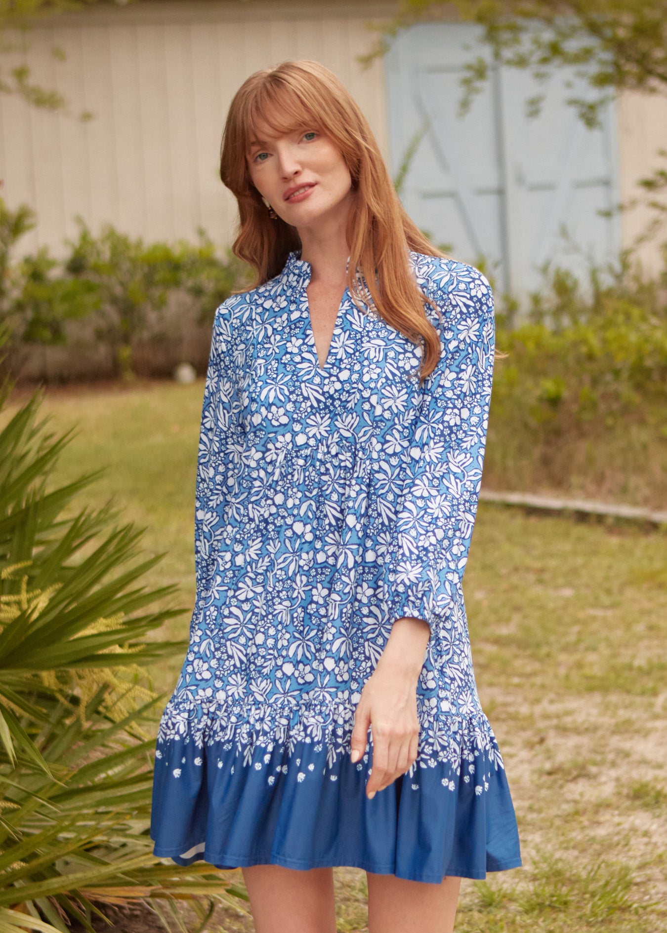 A redhead woman wearing Cabana Life's sun protective Seaside Floral Relaxed Dress walking in front of greenery.