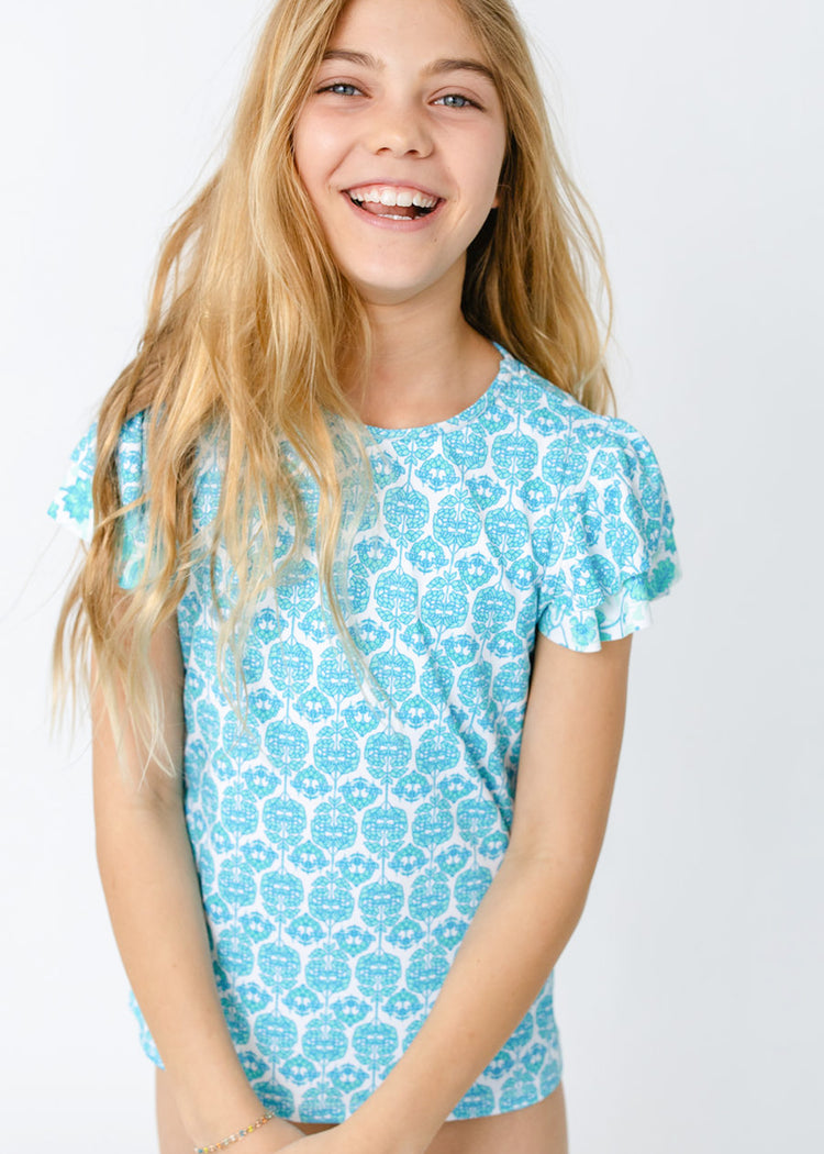 A blonde girl wearing the sun safe Girls Rosemary Beach 3-Piece Short Sleeve Rashguard Set from Cabana Life.