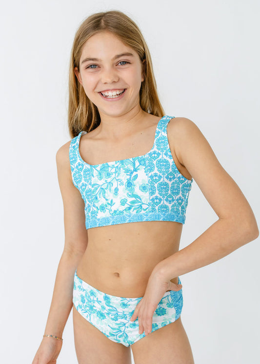 A blonde girl wearing the bikini from Cabana Life's sun safe Girls Rosemary Beach 3-Piece Short Sleeve Rashguard Set.