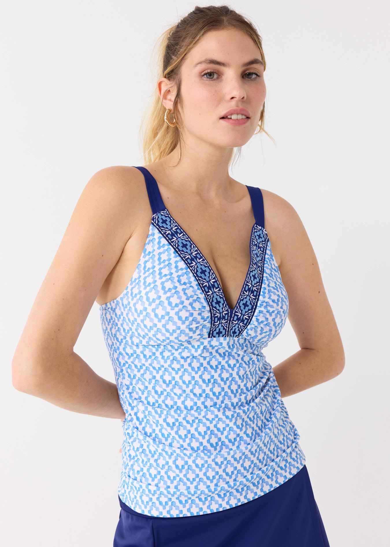 A blonde woman wearing the Cabana Life sun protective Seaside Embroidered Tankini Top and Navy Classic Swim Skirt with gold jewelry.