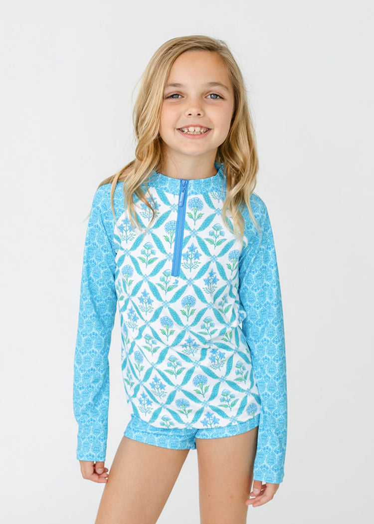 A blonde girl wears Cabana Life's sun safe Girls Rosemary Beach 3-Piece Long Sleeve Rashguard Set.