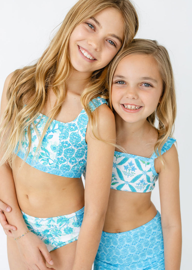 Blonde girls wear bikinis from Cabana Life's sun safe Girls Rosemary Beach 3-Piece Short Sleeve Rashguard Set and Girls Rosemary Beach 3-Piece Long Sleeve Rashguard Set.