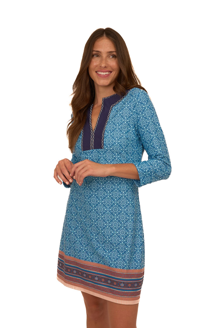 A brunette woman with her hands in front of her chest wearing Cabana Life's sun protective Camden Leaf Embroidered Tunic Dress on a white background.