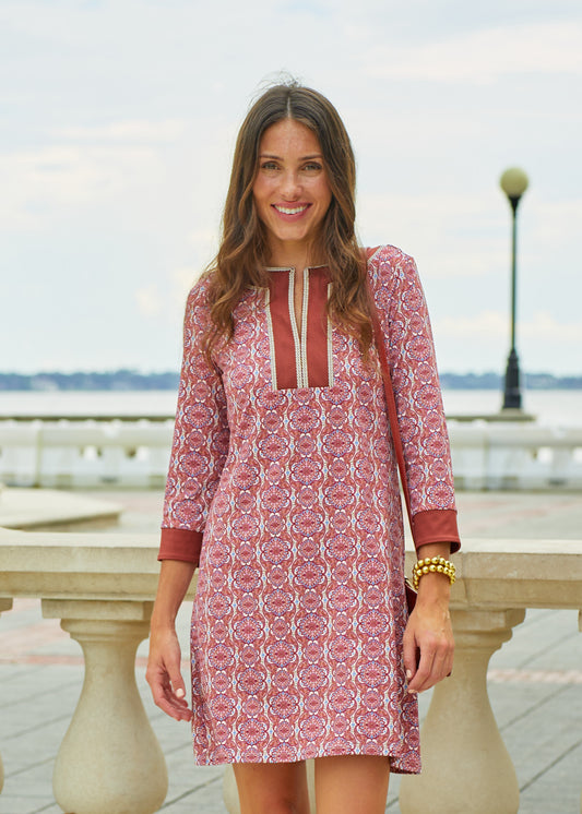 A brunette woman wearing Cabana Life's sun protective Camden Geo Embroidered Tunic Dress in front of a white cement railing in a park.