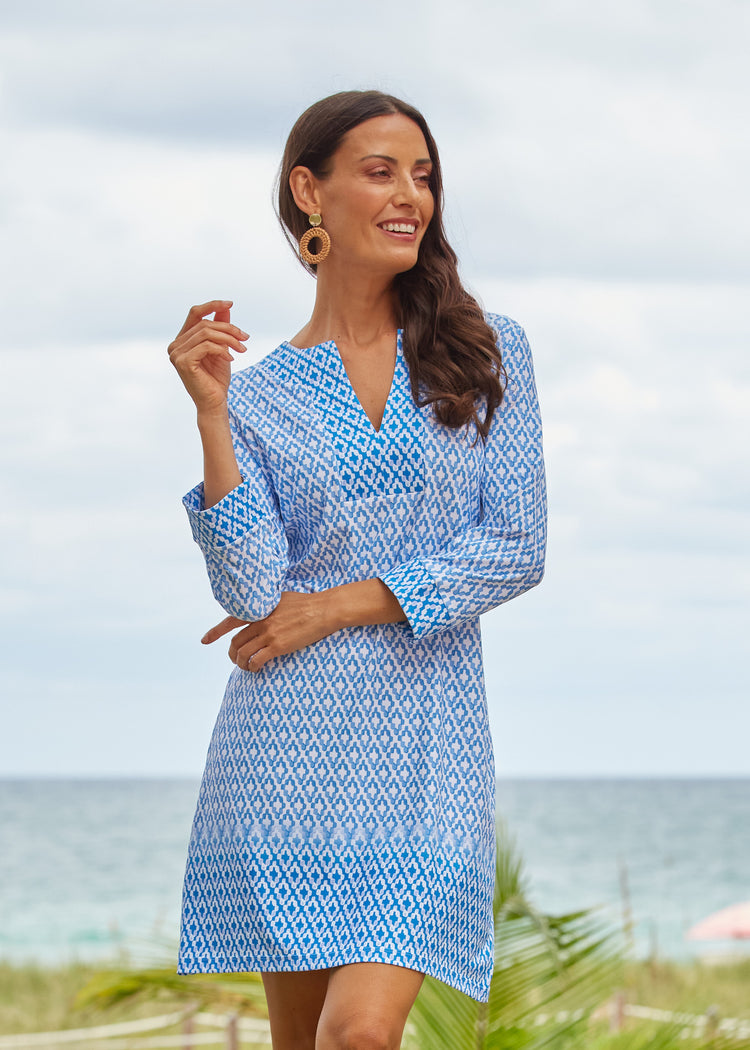 A brunette woman wearing the Cabana Life sun protective Seaside Tunic Dress with arms crossed at an oceanfront resort.