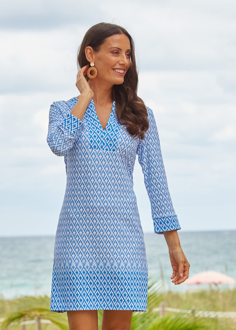 A brunette woman wearing the Cabana Life sun protective Seaside Tunic Dress with an arm up at an oceanfront resort.