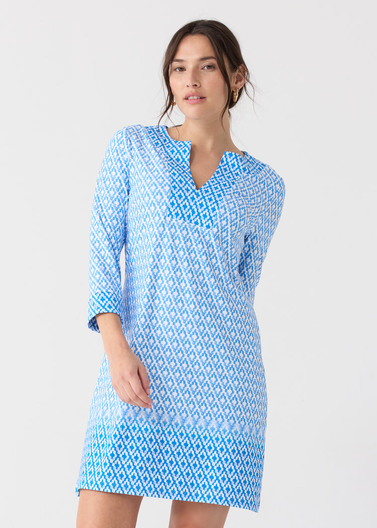 A dark-haired woman wearing the Cabana Life sun safe Seaside Tunic Dress with gold hoops.