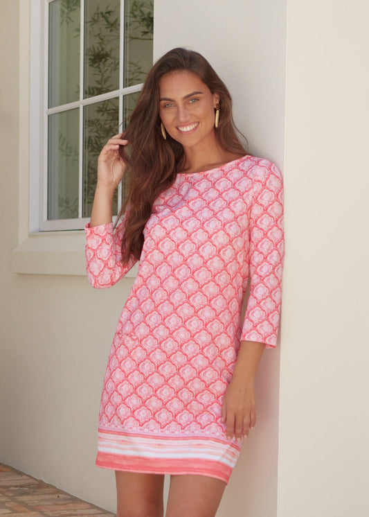 A brunette woman wearing the Cabana Life sun protective Amelia Island Cabana Shift Dress with her hand in her hair against a cream wall.