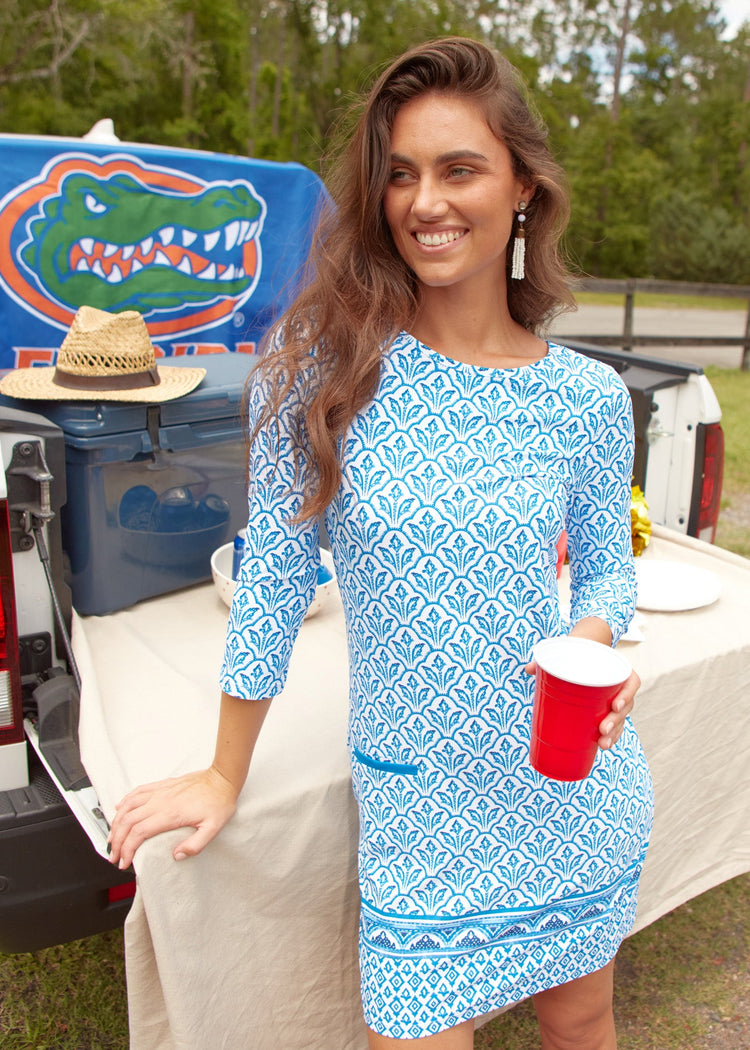 A brunette woman holding a red plastic cup and wearing the sun protective Blue Cabana Shift Dress from Cabana Life in front of University of Florida tailgate setup on a white truck.