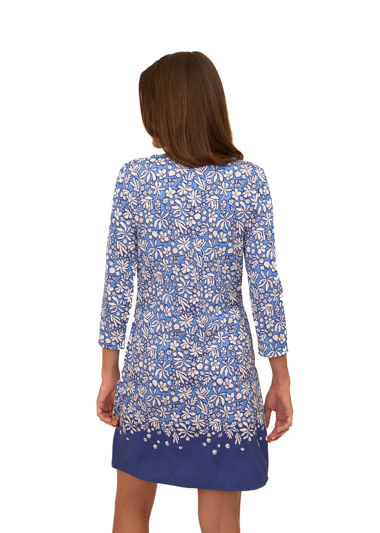 The back of a brunette woman wearing Cabana Life's sun protective Seaside Floral Cabana Shift Dress on a white background.