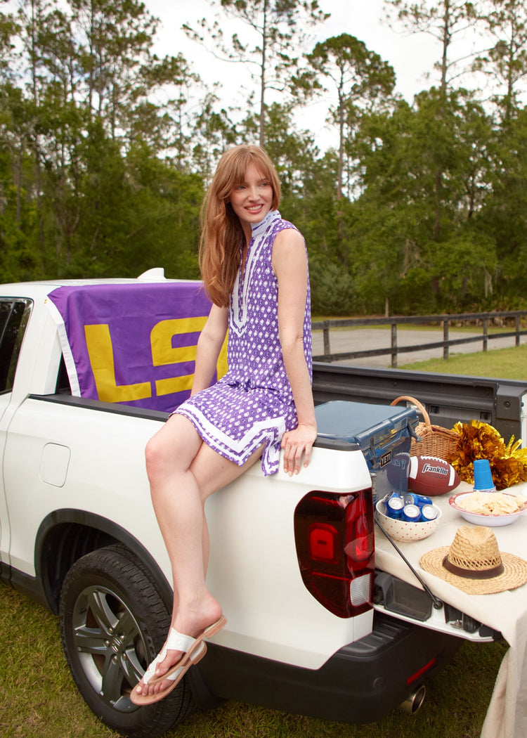 A redhead woman wearing the sun protective Purple Sleeveless Tunic Dress from Cabana Life with sandals while sitting on the side of a white truck.