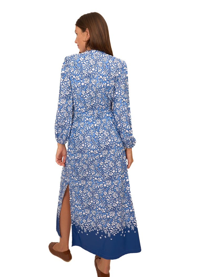 The back of a brunette woman wearing Cabana Life's sun protective Seaside Floral Button Down Maxi Dress with her leg out of bottom dress slit on a white background.