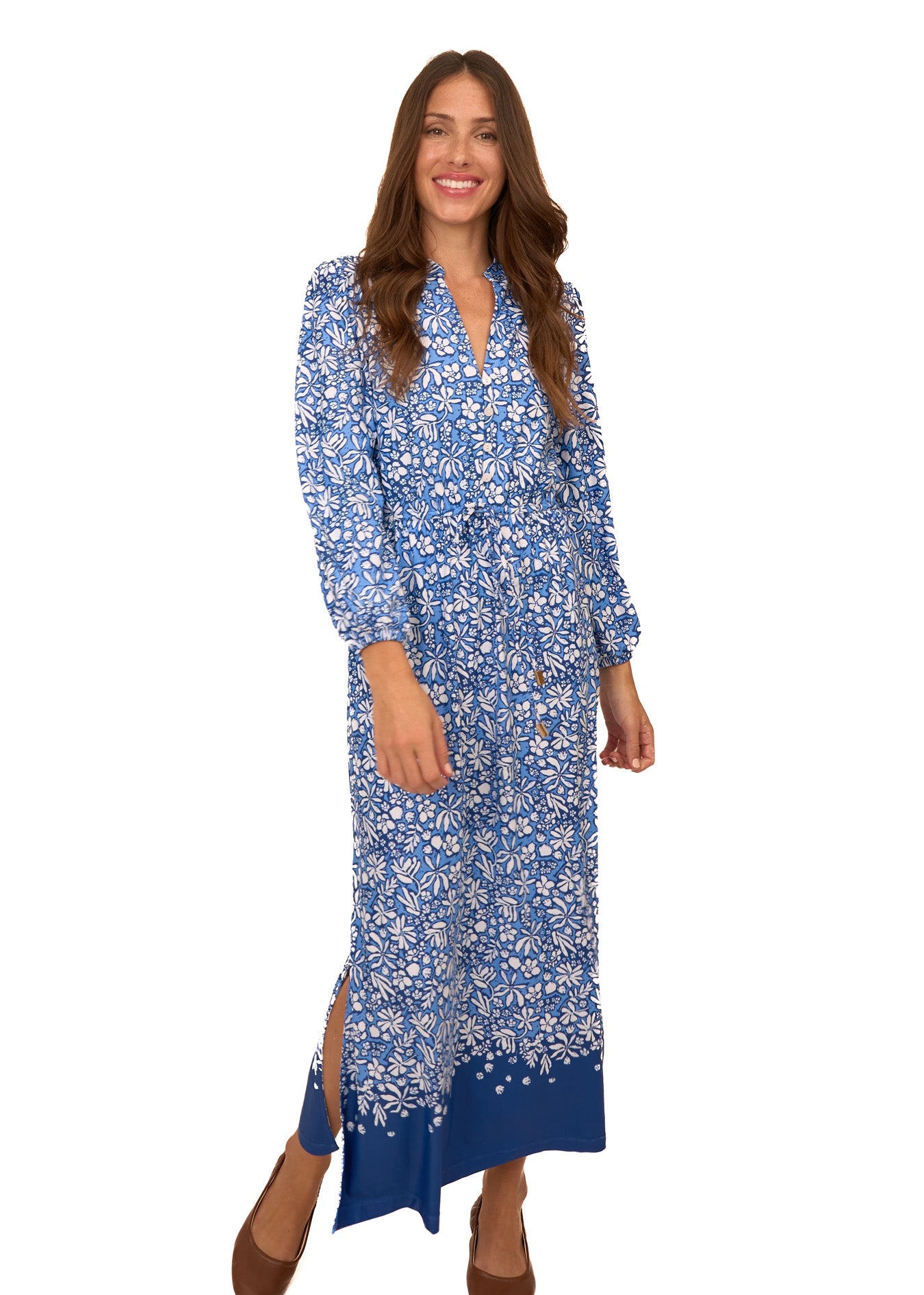 A brunette woman wearing Cabana Life's sun protective Seaside Floral Button Down Maxi Dress with brown ballet flats on a white background.