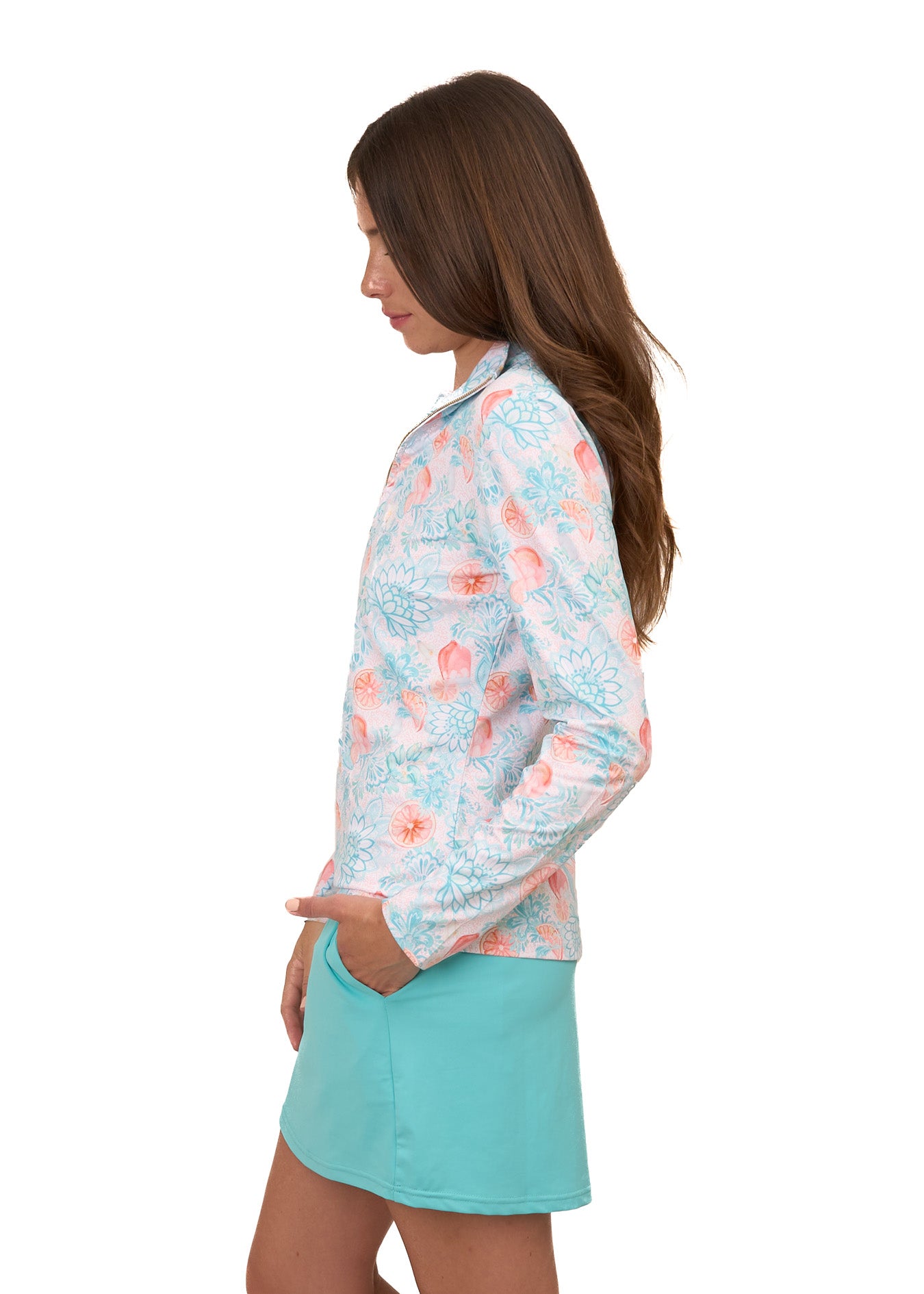 The side of a brunette woman wearing Cabana Life's sun protective Spritz 1/4 Zip Sport Top and Aqua Skort on a white background.