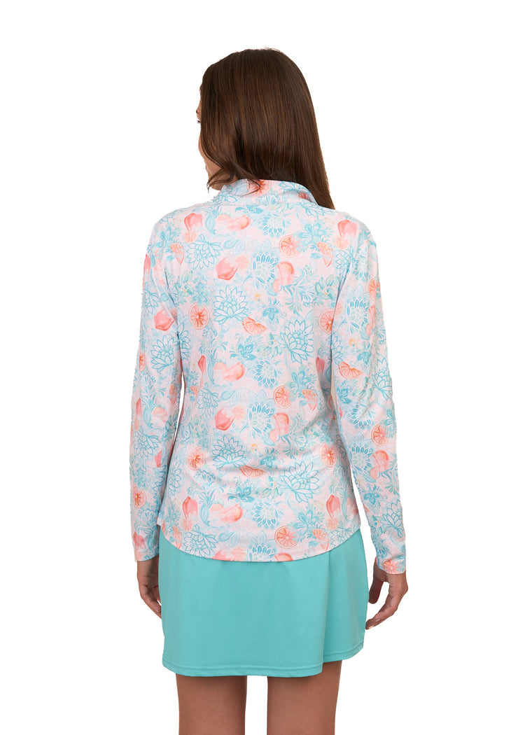 The back of a brunette woman wearing Cabana Life's sun protective Spritz 1/4 Zip Sport Top and Aqua Skort on a white background.