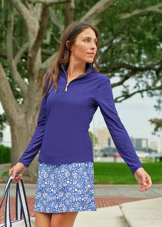 A brunette woman wearing the sun protective Navy 1/4 Zip Sport Top and navy floral patterned Seaside 17" Skort from Cabana Life walking in a park.