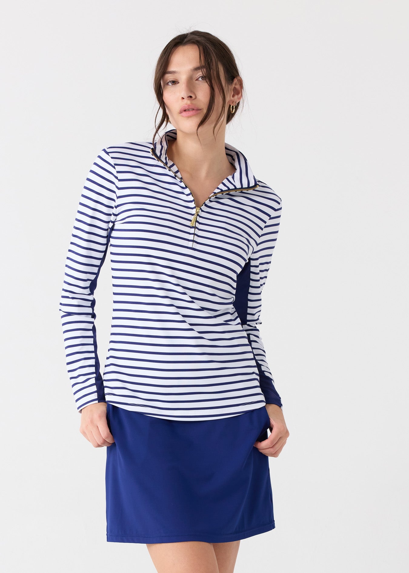 A woman wearing the Cabana Life sun protective Navy Stripe 1/4 Zip Sport Top with hands in pockets of the Navy 17" Skort.