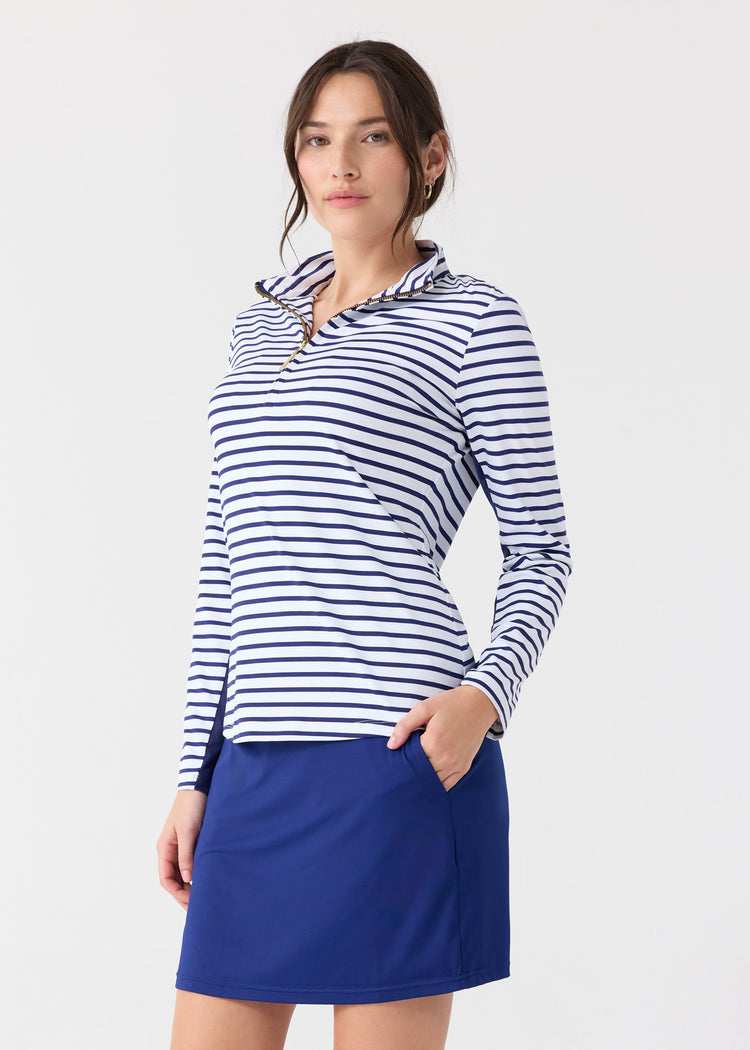 A woman wearing the Cabana Life sun protective Navy Stripe 1/4 Zip Sport Top with a hand in the pocket of the Navy 17" Skort.