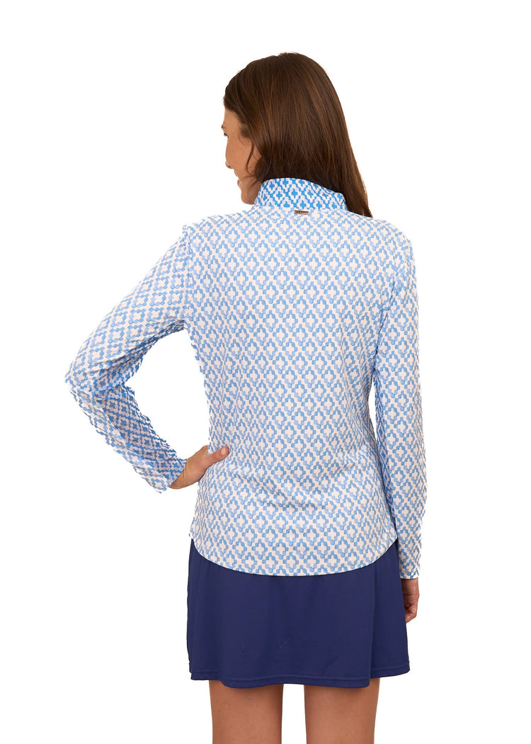 The back of a brunette woman wearing the Cabana Life sun protective Seaside 1/4 Zip Sport Top and Navy 17" Skort with a hand on her hip on a white background.