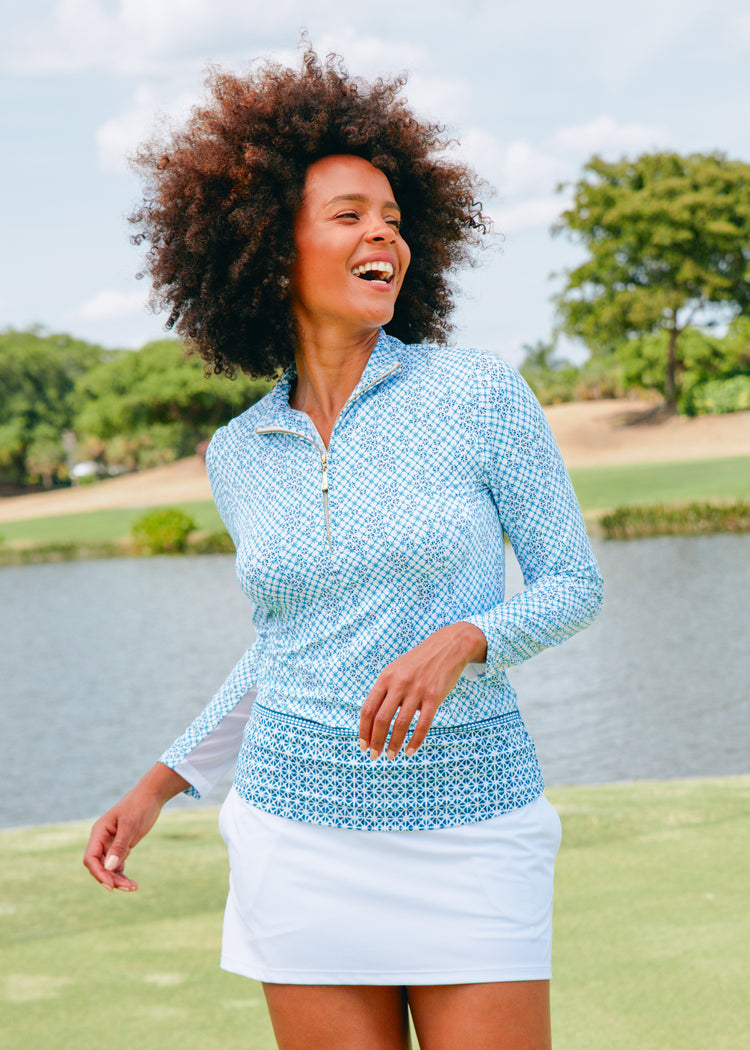 A black woman running on golf course laughing while wearing the Cabana Life sun protective Sag Harbor 1/4 Zip Sport Top and White Skort.