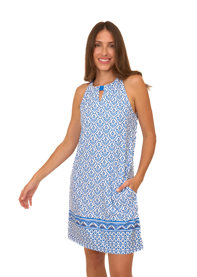 A brunette woman wearing Cabana Life's sun protective Blue Game Day Sleeveless Shift Dress with her hand in her pocket on a white background.