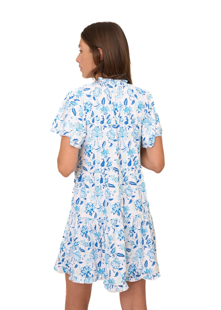 The back of a brunette woman with her arms in front wearing the sun protective Bubbly Short Sleeve Tiered Ruffle Dress from Cabana Life on a white background.