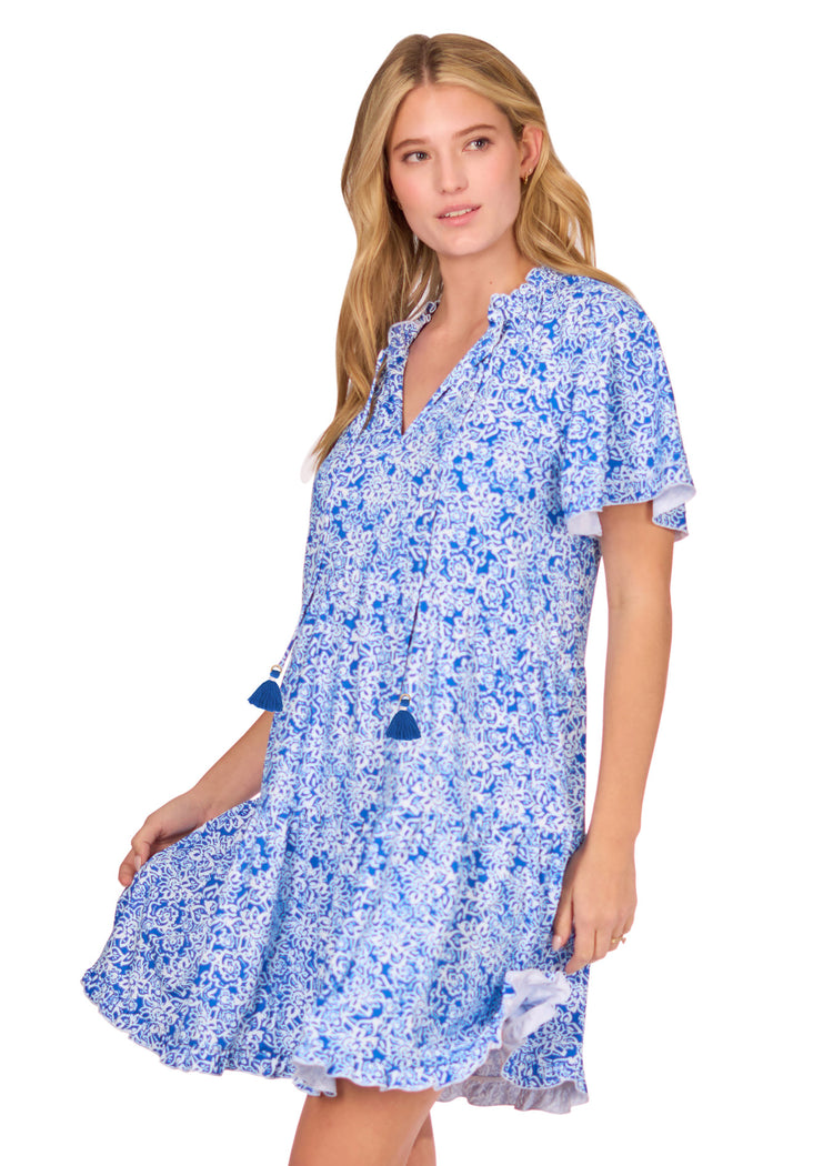 The side of a blonde woman on a white background holding the skirt of the Blue Game Day Short Sleeve Tiered Dress from Cabana Life's Sun Protective Line.