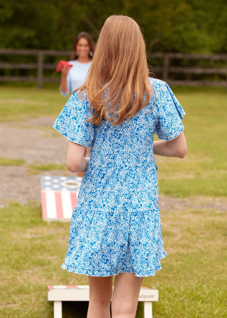 The back of a redheaded woman wearing the sun protective Cabana Life Crimson Short Sleeve Tiered Dress playing cornhole on the grass.