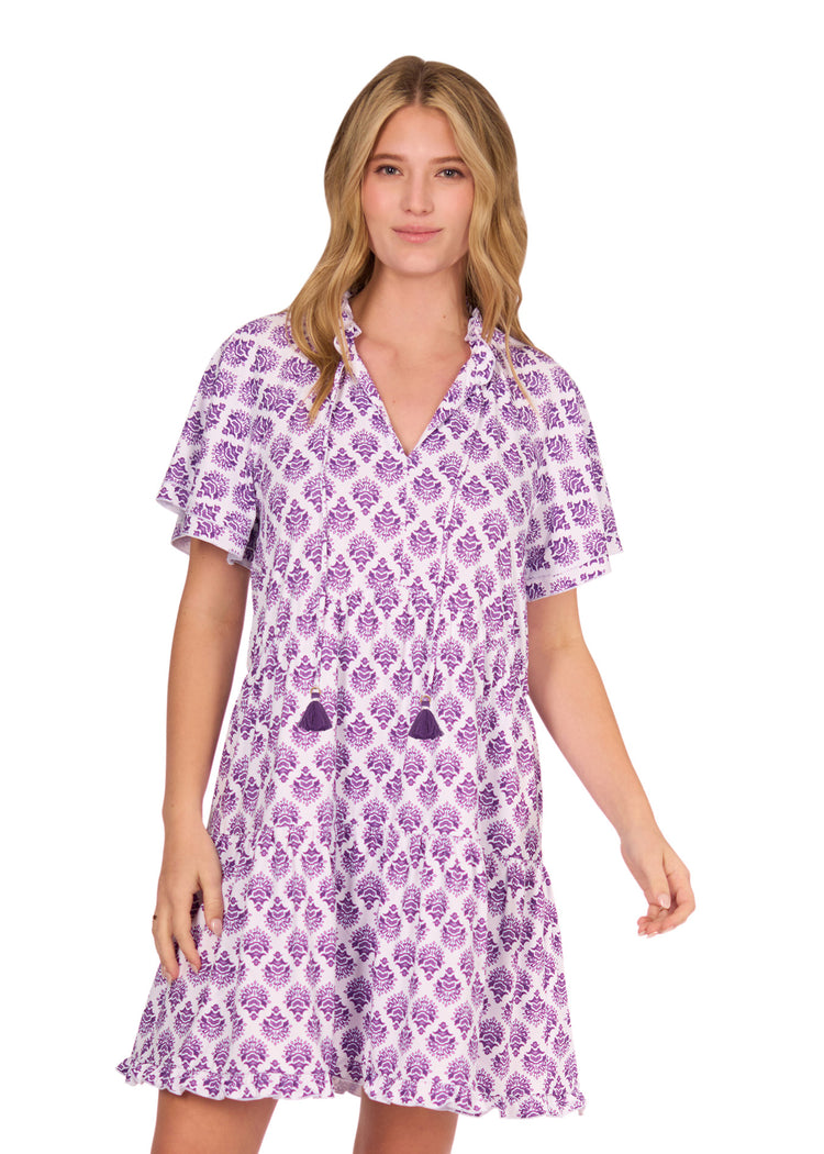 A blonde woman wearing the sun protective & flowy Purple Short Sleeve Tiered Dress from Cabana Life on a white background.