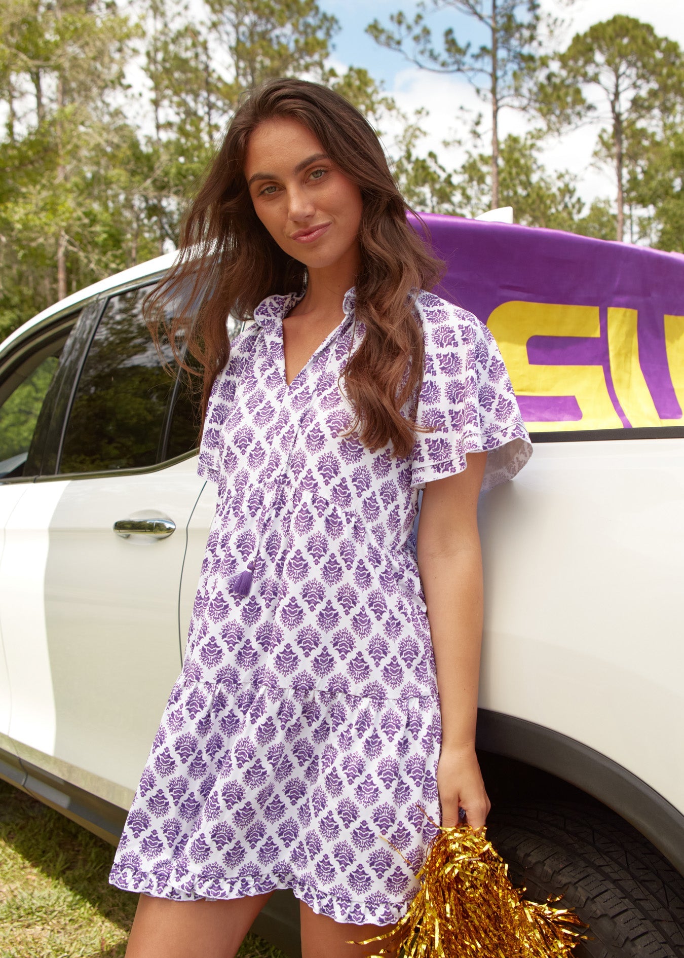 A brunette woman wearing the sun protective Cabana Life Purple Short Sleeve Tiered Dress in front of a white truck.