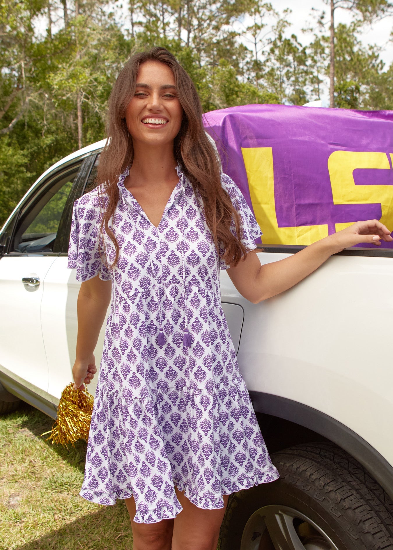 A brunette woman smiling while wearing the sun protective Cabana Life Purple Short Sleeve Tiered Dress in front of a white truck.