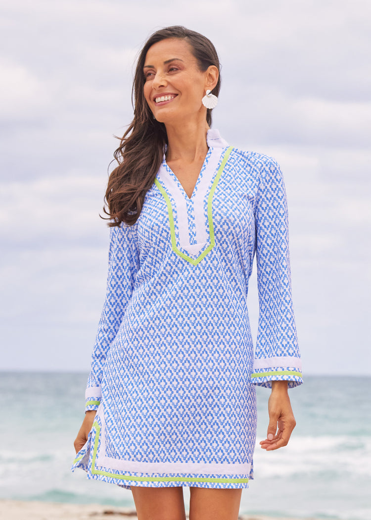 A brunette woman smiling and walking on the beach wearing the Cabana Life sun protective Seaside Pique Tunic Dress.