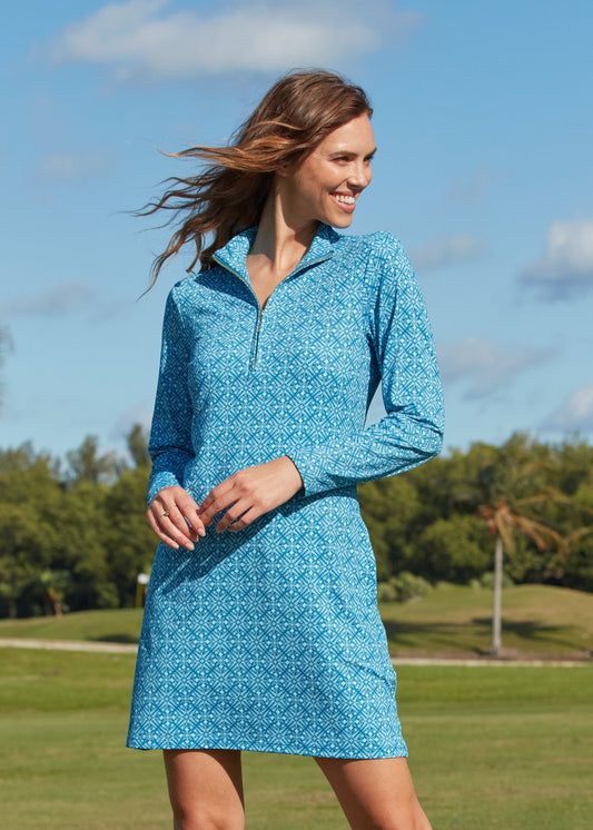 A brunette woman looking to the side while wearing the sun protective and turquoise printed Camden 1/4 Zip Sport Dress from Cabana Life on a golf course.