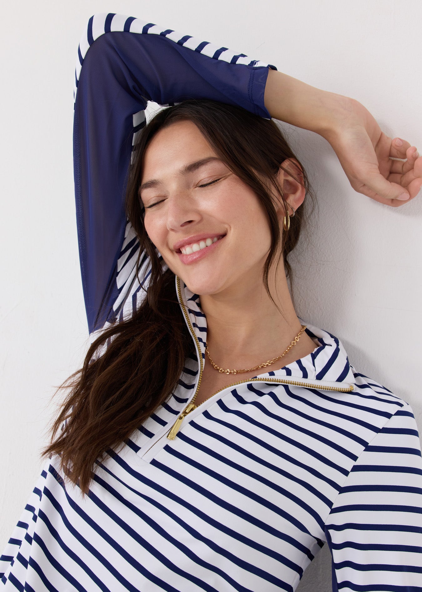 A dark haired woman closing her eyes while wearing the Cabana Life sun protective Navy Stripe 1/4 Zip Sport Dress with navy mesh underarm venting and gold jewelry.