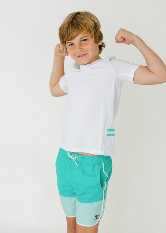 A boy with his arms up wearing the sun protective Boys White Side Stripe Rashguard and Boys Aqua Colorblock Swim Trunk from Cabana life.