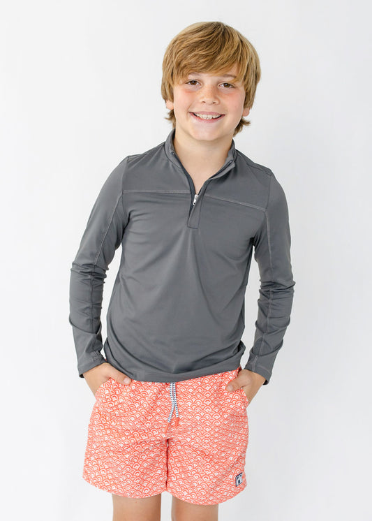 A boy wearing the sun protective Boys Grey Sport Zip Top and Boys Amelia Island Swim Trunk from Cabana Life.